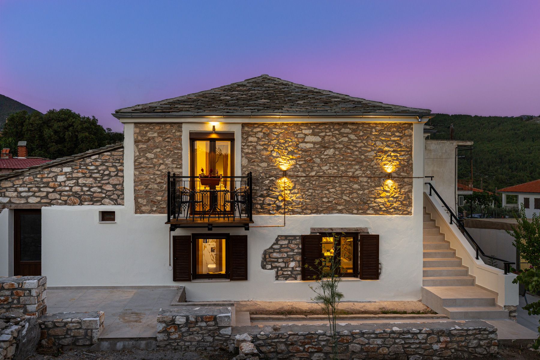 The front elevation at dusk, windows warm against the stone
